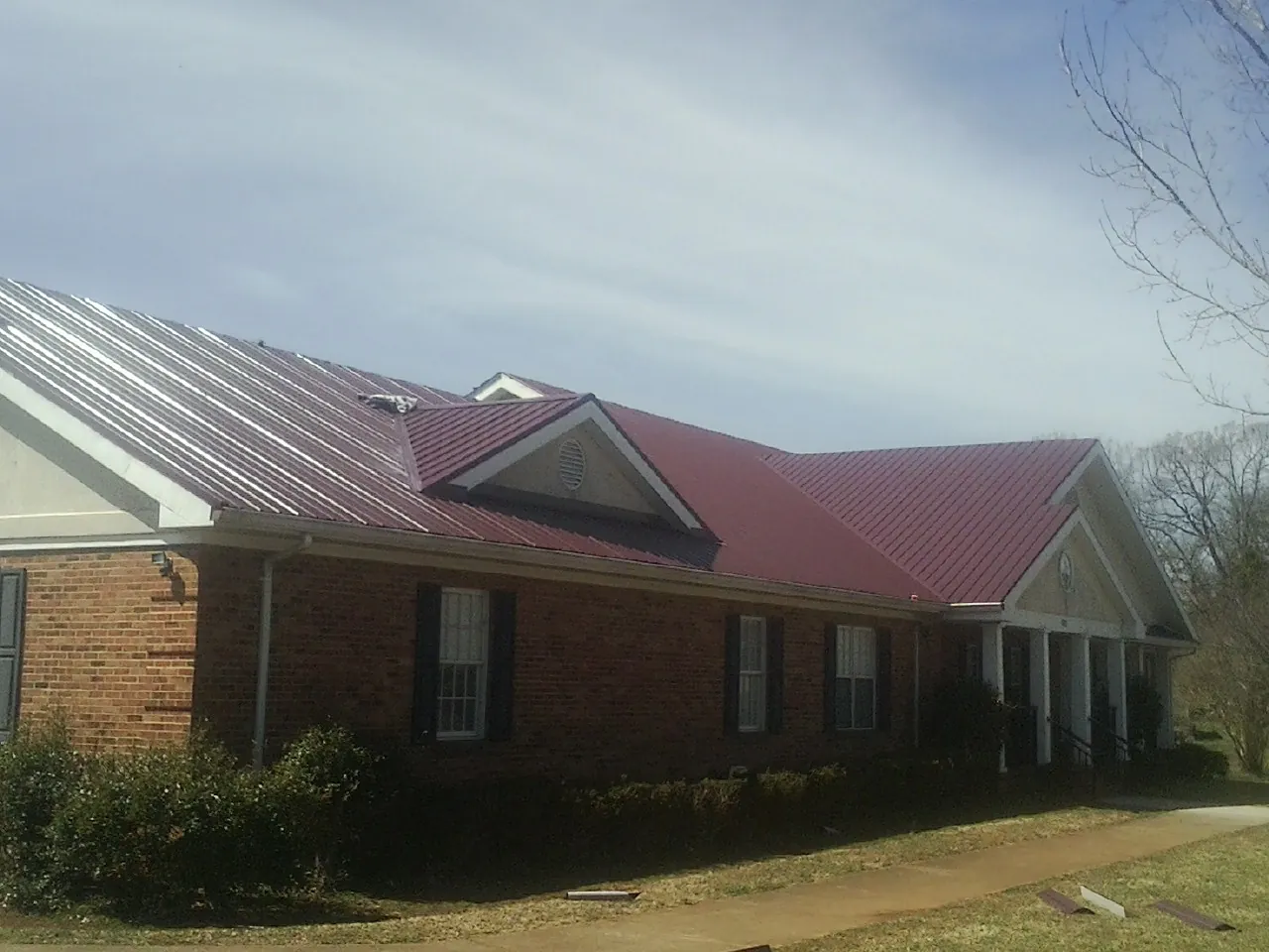 Red metal roof with gabled entries on a long brick building, from a Hail Damage Roof Repair job in Russellton