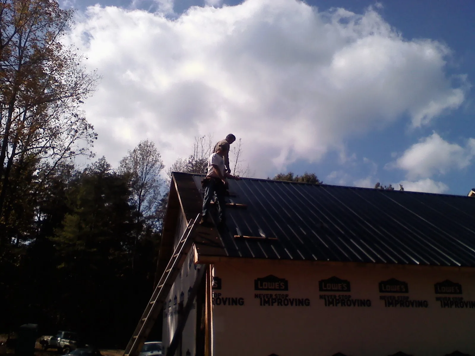 Roofer fastening dark metal panels high against a cloudy sky, from a Roof Inspection job in Russellton