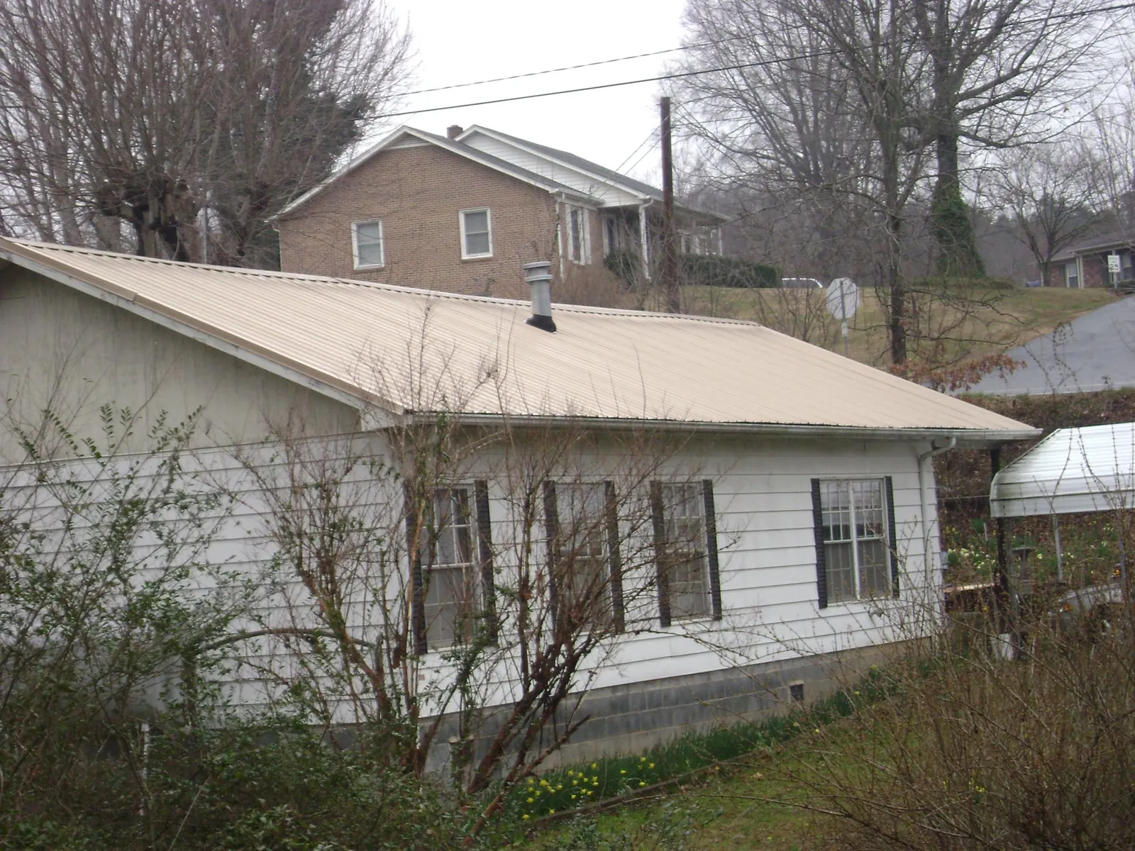 Tan metal roof on a white sided house set into a hillside — Commercial Roofing by Roofing Brothers in Russellton